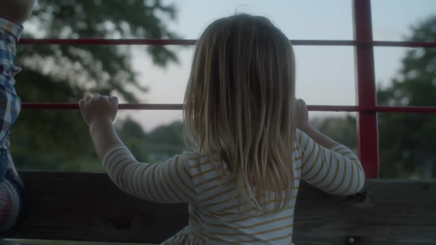 A blonde little girl sits looking at the scenery while holding onto a red railing