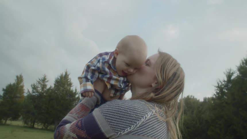 Woman playing with a baby on a field near a cow