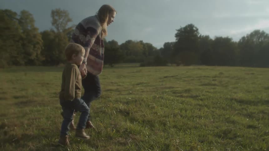 A woman holds her sons hand as their run toward horses grazing in a field