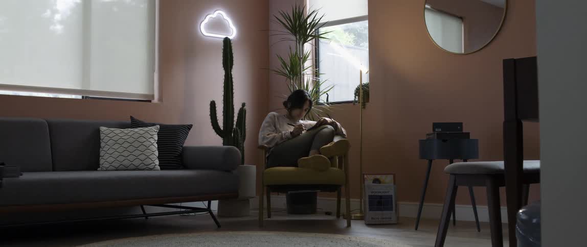A woman writes and sits with her legs pulled up in a chair in her living