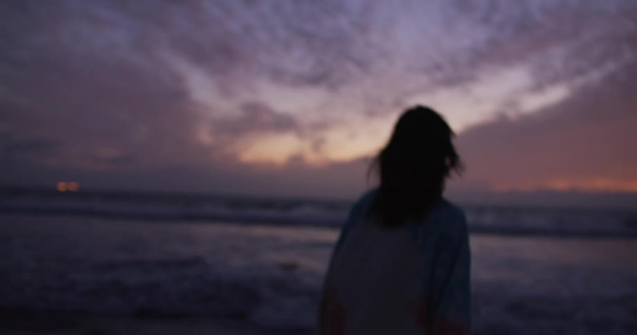 A woman is jumping around on the beach at sunset