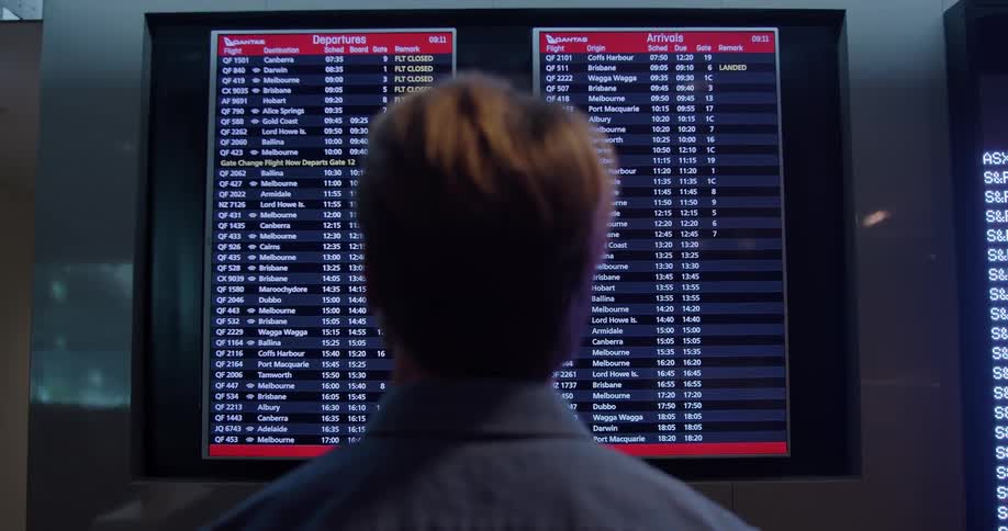 A man stands in front of a departure and arrival board
