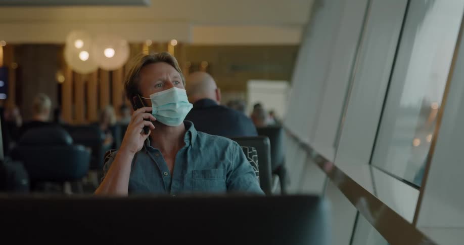 Man wearing a face mask talking on a smartphone waiting in an airport lounge