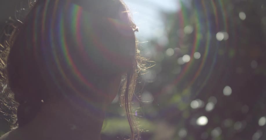 A woman with long hair walks outdoors next to trees on a sunny day