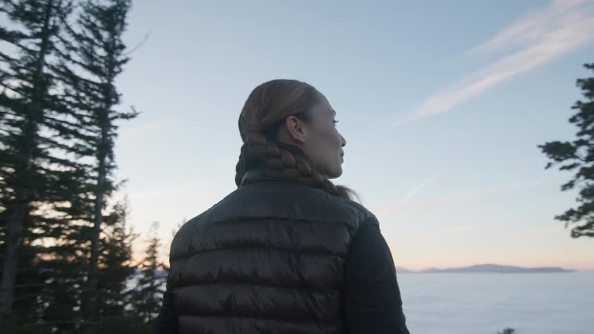 A woman standing on top of a hill looking down onto a field of clouds