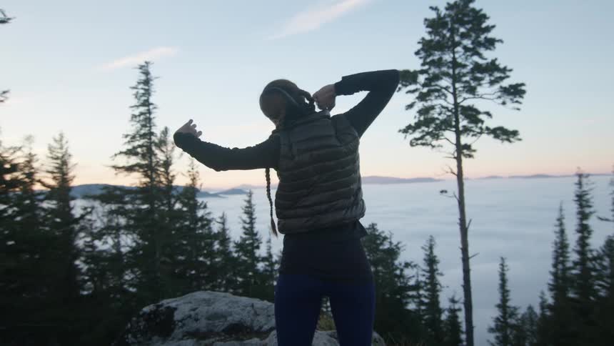 A woman climbs out of a tent and stretches while looking out at the horizon at sunrise