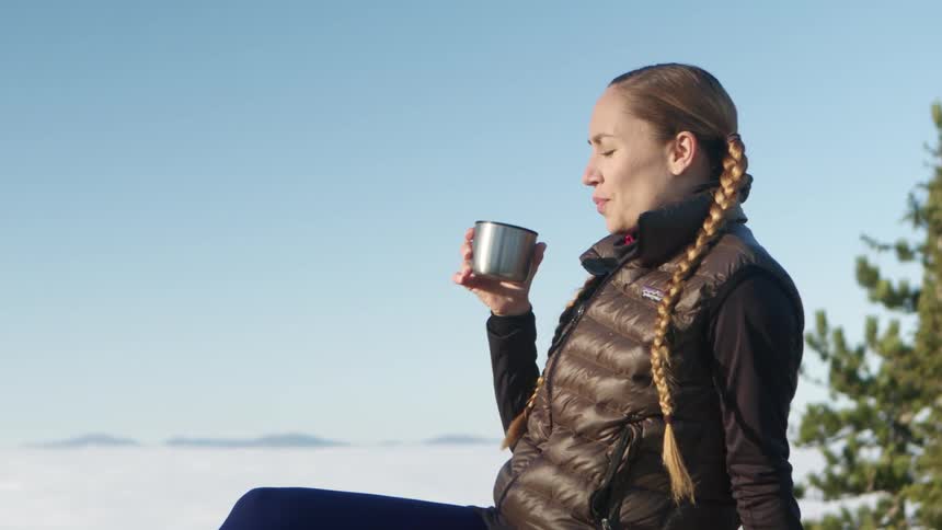 A woman squints and shades her eyes as she sips coffee on a bright winter day