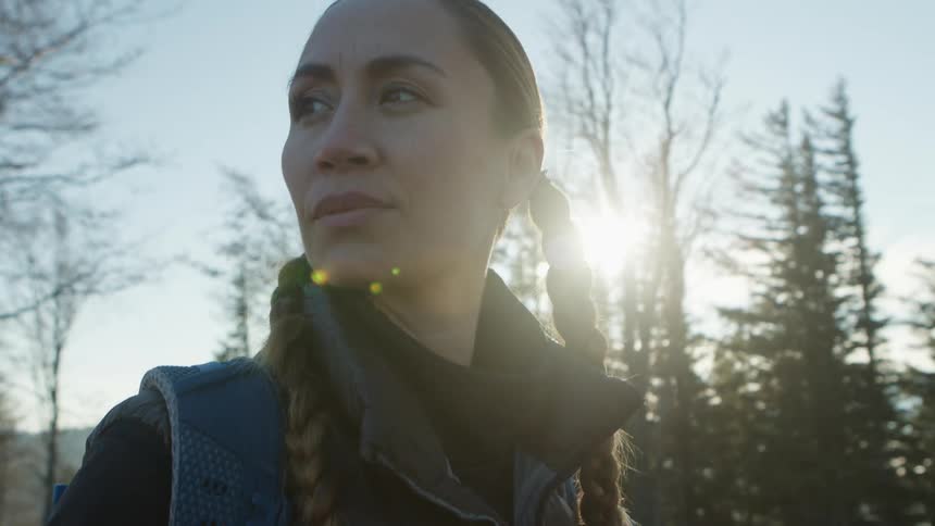 Young woman wearing pigtails looking around in the pine forest at sunset