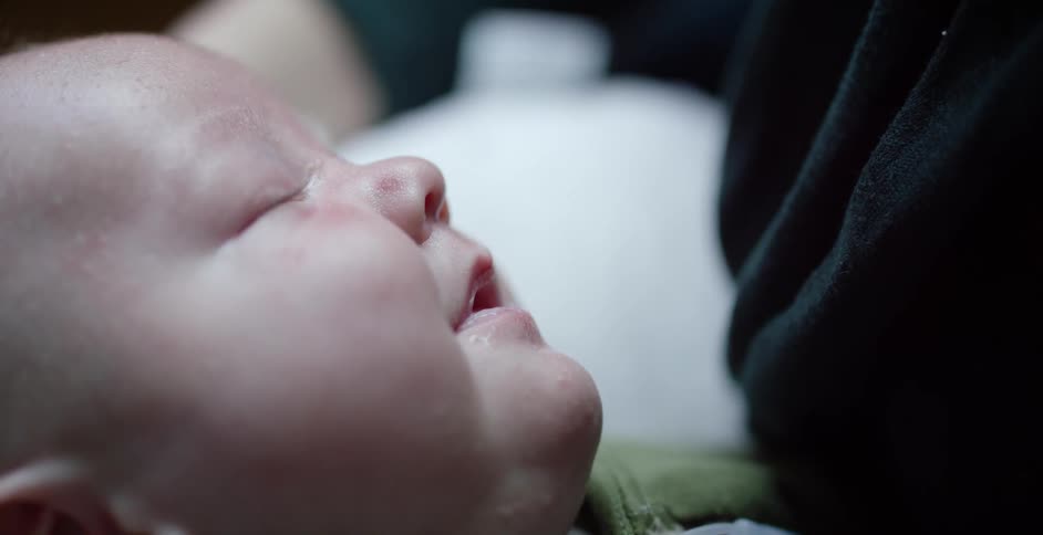 A baby lies with his eyes closed as his mouth crinkles slightly as he dreams