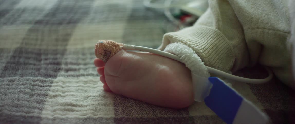 A baby is lying on a blanket with a tube attached to the toe