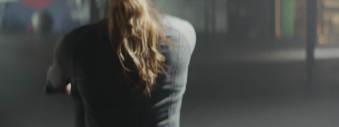 Young fit woman using a static rowing machine on a dimly lit gym