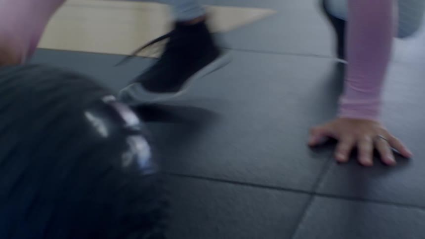 Woman pushes exercise ball across floor mats at gym