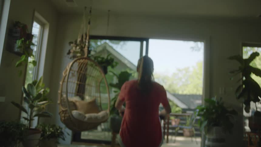 A woman pulls the bar on a rowing machine sitting in a room facing a large patio door