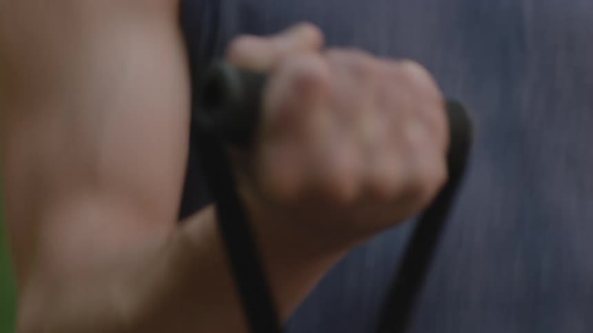 A male teenager is exerting himself pulling weights on his right arm outdoors