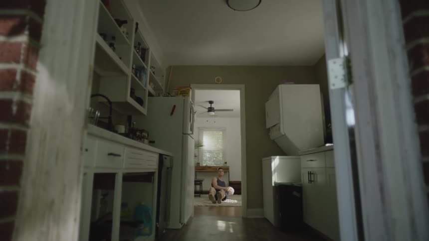 Through a doorway a person can be seen exercising while sitting on the floor of their home