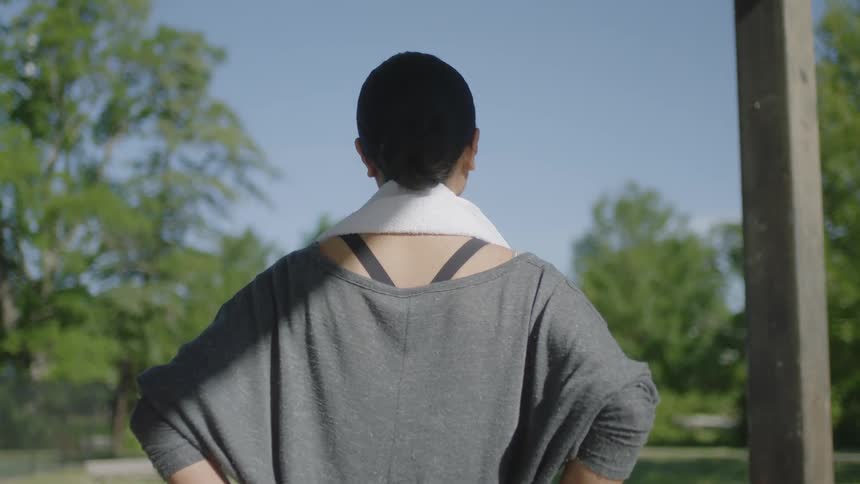 A woman standing with a towel around her neck with trees the sky and clouds in the background