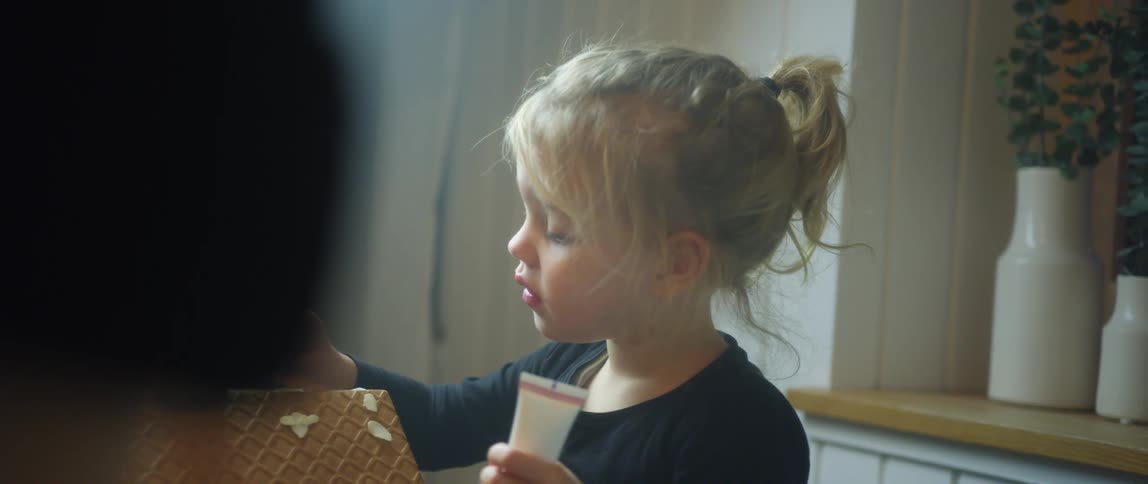 Little blonde girl decorating a gingerbread house with icing