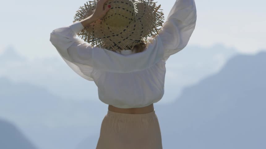 Woman wearing a hand woven sun hat standing outside looking out towards a mountain range