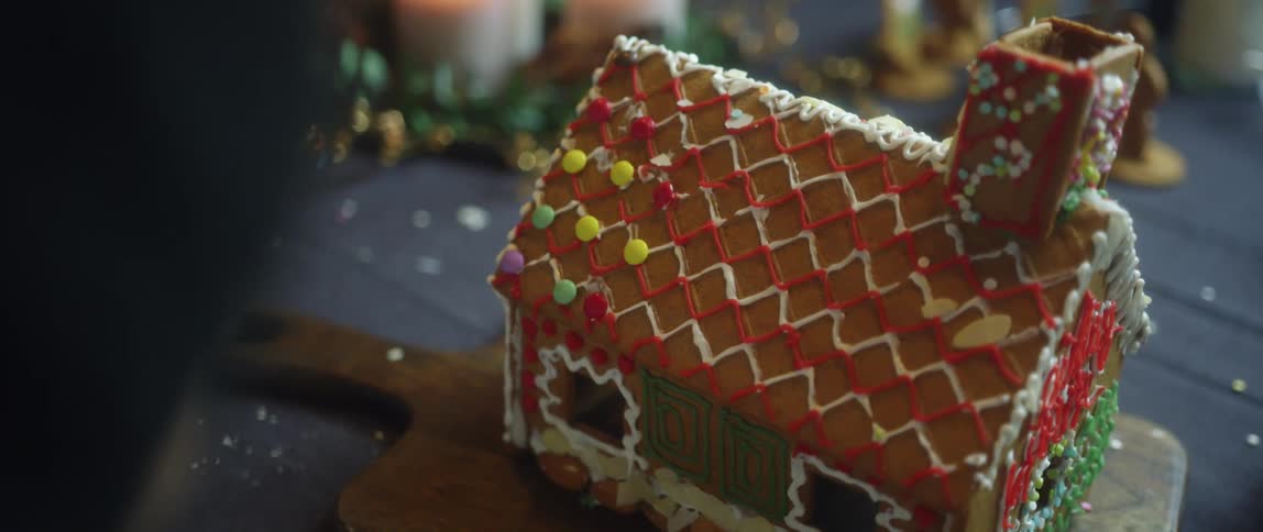 A young girl adds round candy to the roof of a frosted gingerbread house