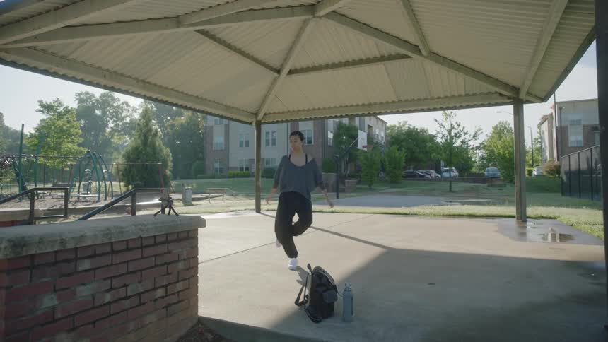 A woman stands outside under an awning and dances