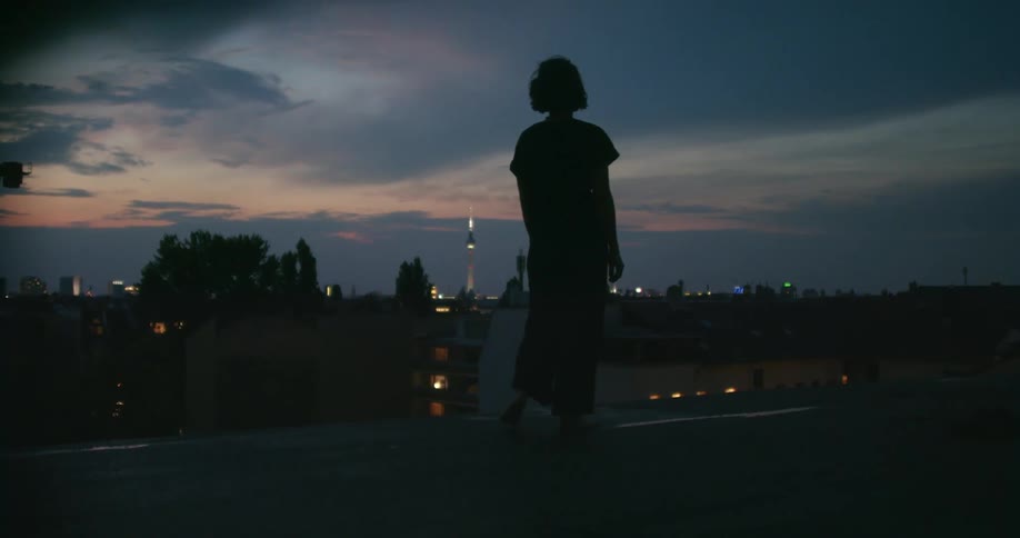 Young woman walking on the edge of a building roof in the city at sunset