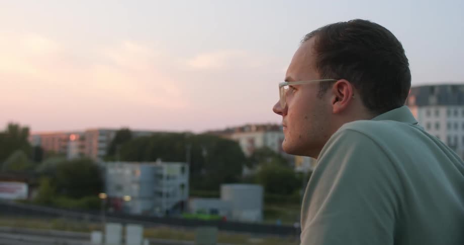 Man reclined on the railing of a pedestrian overpass looking at the sunset over the city