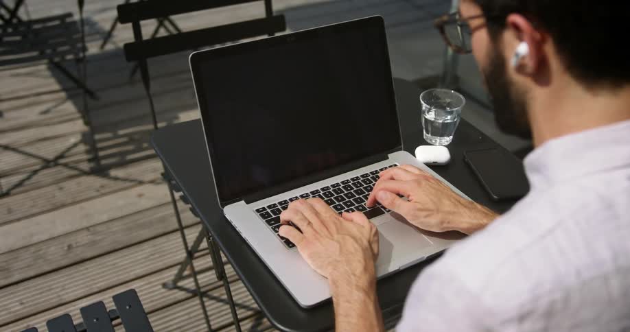 A man with glasses sitting at a table typing on a laptop