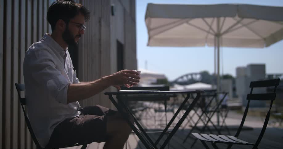A man walks on to a patio at a restaurant and sets down a glass of water and his laptop and opens it
