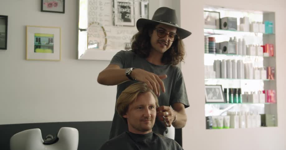 A man sits in a chair in a hair salon while another man gets ready to cut his hair
