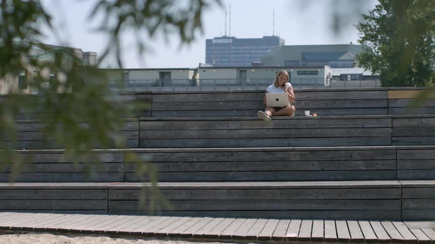 A woman is sitting outside and typing on a laptop