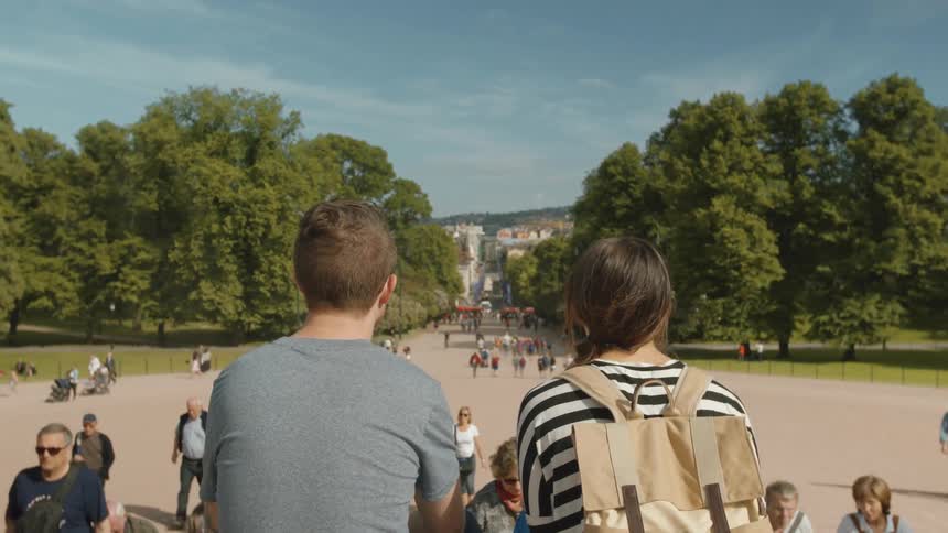 A man and woman sit on steps in a large park facing away from the camera