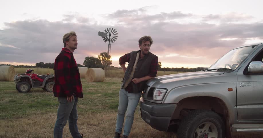 Two men are talking outdoors by a vehicle