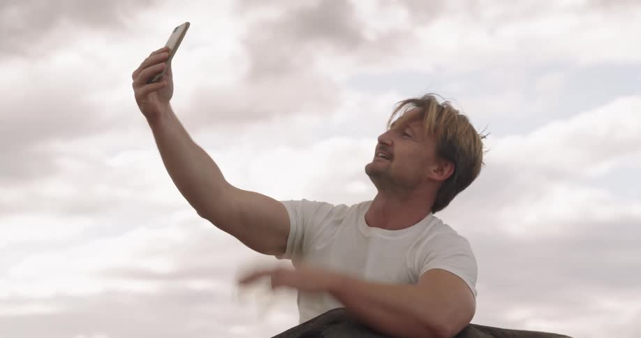 A man sits with his dog while making a video on his cellphone