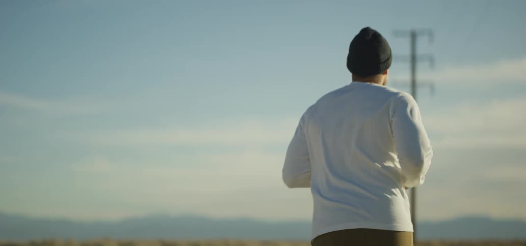 A man wearing a beanie jogs outdoors on a sunny and windy day