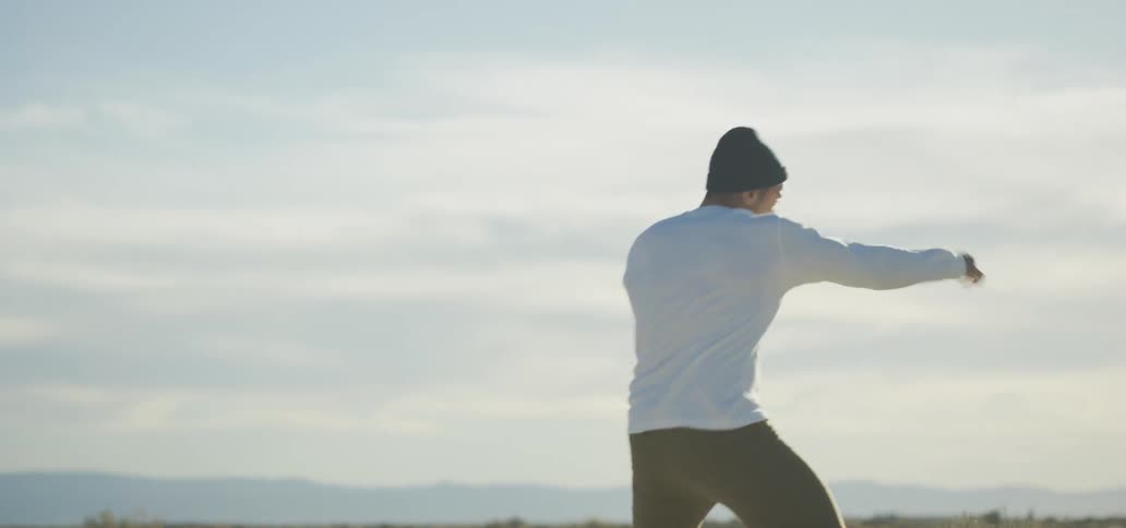 A man practices boxing moves by throwing punches in a field outside