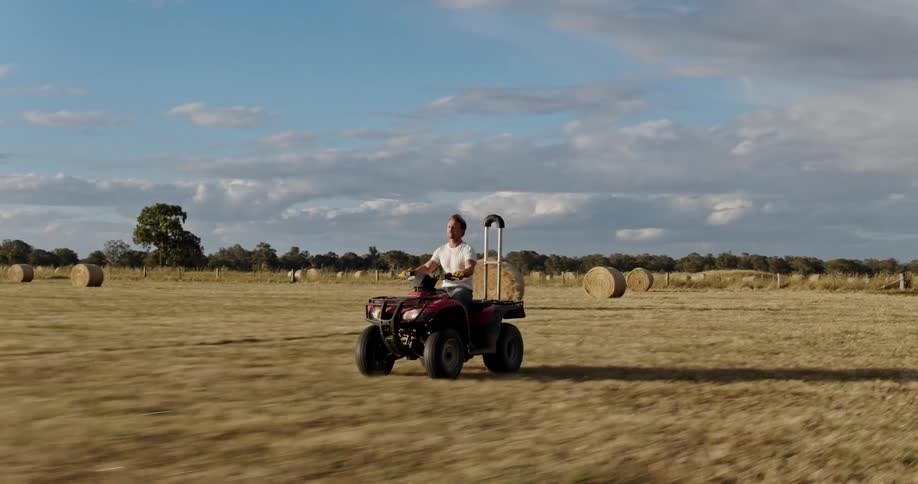 Man drives four wheeler through field with rolled hay bales
