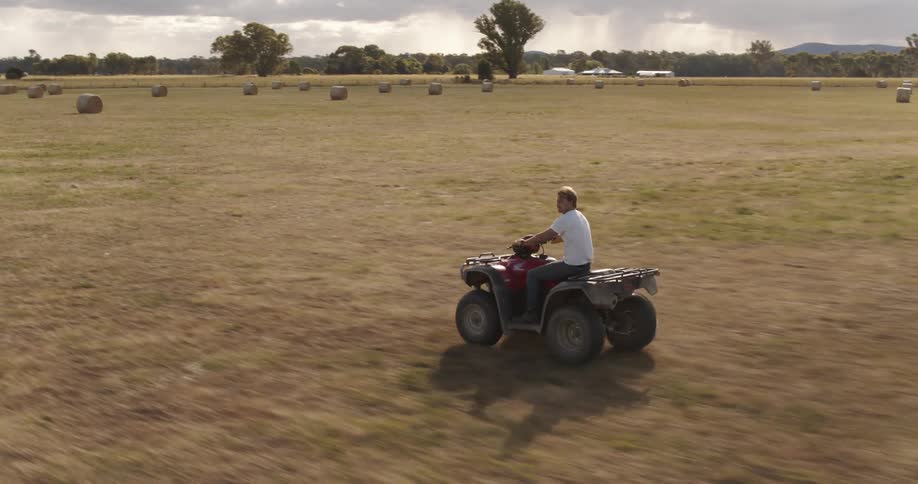 A man rides an atv on farmland with bales of hay