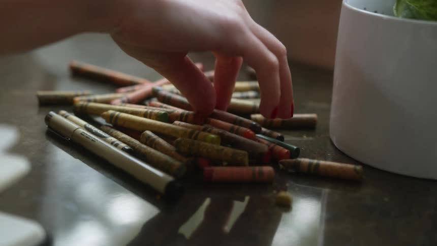 A female reaches out and retrieves a crayon from a reflective tabletop