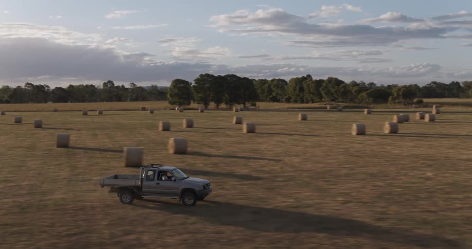 A gray truck driving over a rural field with hay bales