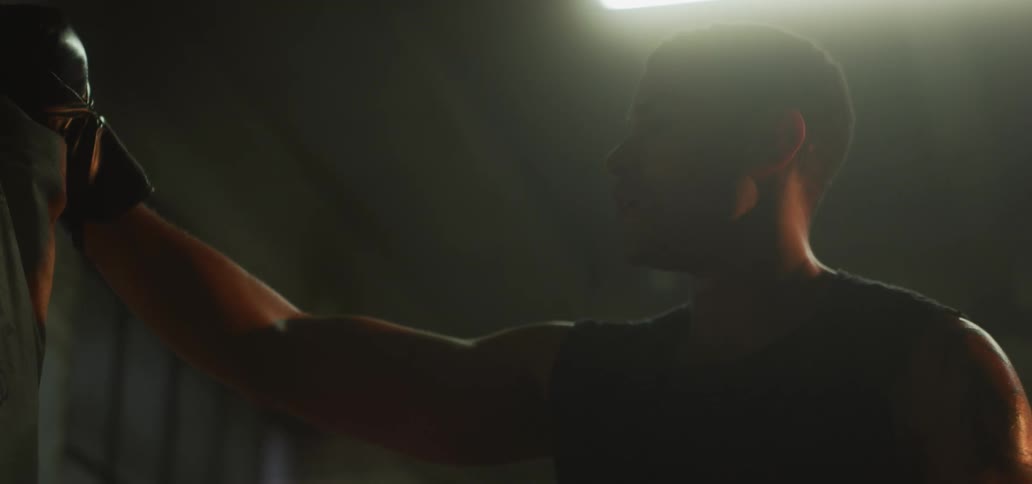 A boxer takes a break from training and rests his gloved hand against a boxing bag