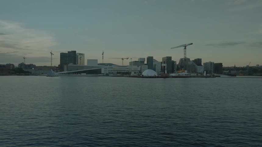 A city on a harbor with construction cranes under slightly cloudy skies