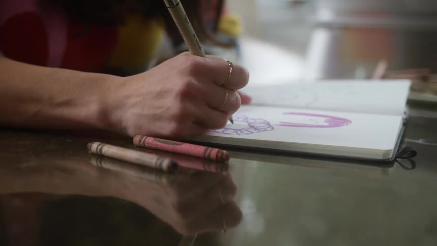 A woman sitting at a table uses a marker to draw in a noteboard