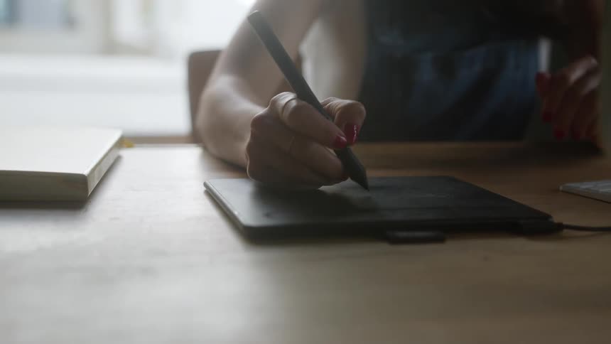 A person is seated in front of a table and is using a stylus to write on a tablet