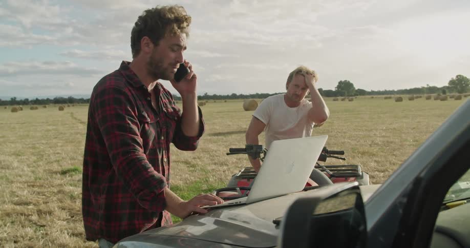 Two men looking at a laptop while one talks on a phone