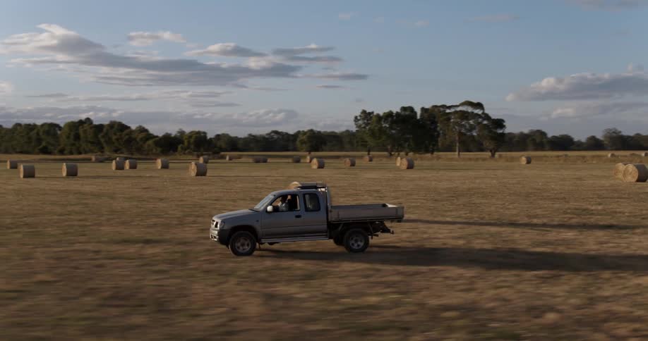 A truck drives along a farmland dotted with bales of hay