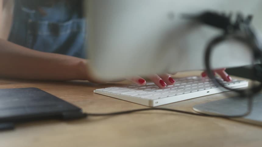 Woman typing on a white keyboard on a desktop computer at a desk indoors