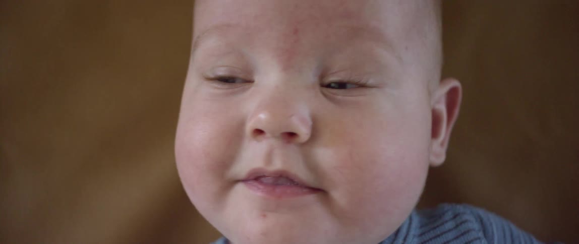 A smiling baby sticking its tongue between its lips while lying on a cloth