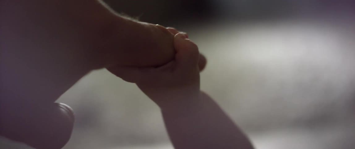An infant grasps the finger of an adult