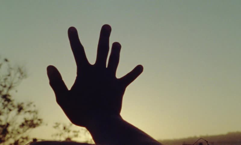 A person is reaching up at the dusk sky