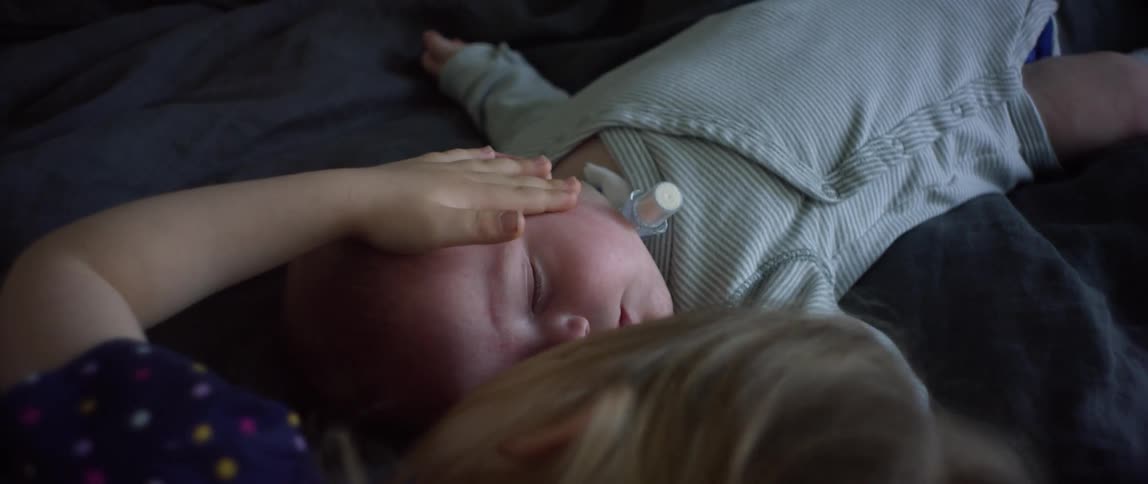 A girl touches a sleeping baby in the bed